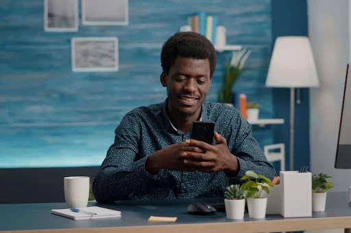 Man smiling while checking social media analytics on his phone at a desk